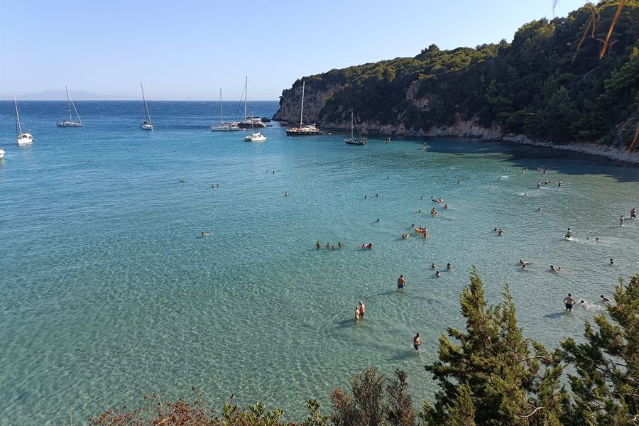 Boats at anchor and swimmers in a clear turquoise cove of the Ionian coast
